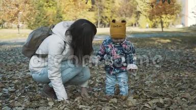 快乐的母女俩一起玩秋叶，一起玩得开心.. 嬉戏的女孩和她的母亲扔树叶